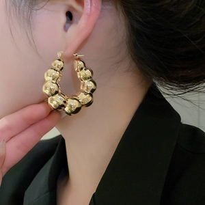 Close-up of a model wearing chunky gold bubble hoop earrings with a high-polished mirror finish
