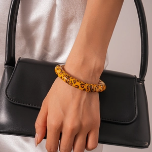 Close-up of leopard print acrylic bracelet in vibrant orange worn with a black leather bag