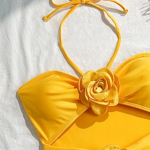 Close-up of bright yellow halter swimwear top with 3D floral applique on white fabric