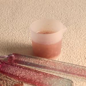 Nahaufnahme eines 30-ml-Silikon-Messbechers mit pinkfarbenen Glitzer-Lesezeichen aus Harz