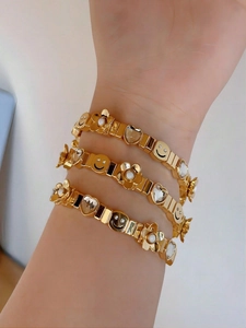 Detail of stacked gold bracelets featuring smiling face, crystal heart, and flower charms