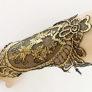 Detail view of gothic black lace arm cuff with baroque gold embroidery on mesh fabric