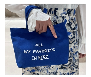 Detail of blue canvas mini tote bag with white text held by model in dress