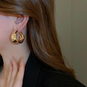 Close-up of polished gold-plated double-layer C-shaped hoop earrings on a female model