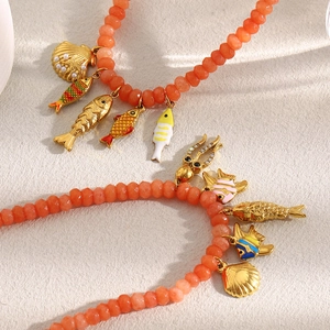Detail of beaded bracelet with 18K gold-plated fish and shell charms on textured surface