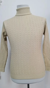 Dettaglio ravvicinato del maglione beige a dolcevita con classiche trame in maglia a treccia