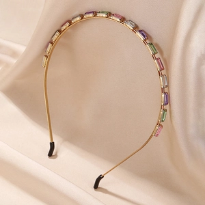Detailed view of golden headband with colorful rectangular gemstones on beige fabric