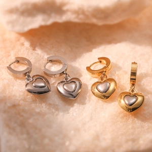 Minimalist heart-shaped drop earrings in gold and silver finish on natural stone background