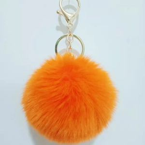 Detailed close-up of vibrant orange faux rabbit fur pompom with golden metal clasp