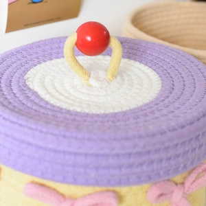 Detail of woven cotton rope storage lid with purple trim and red pom-pom handle