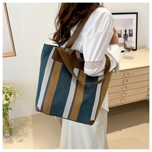 Detailed view of striped canvas tote bag with brown leather straps in a home setting