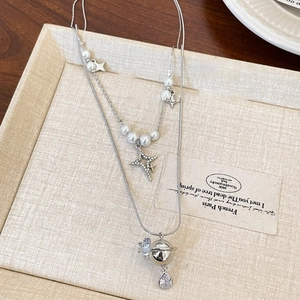 Detailed close-up of double-layer silver necklace with pearl beads and Saturn star pendant