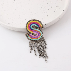 Macro detail of letter S brooch with colorful embroidery and sparkling rhinestone tassels