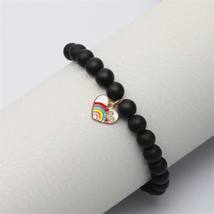 Matte black stone bead bracelet featuring a gold-edged rainbow heart charm on a display stand