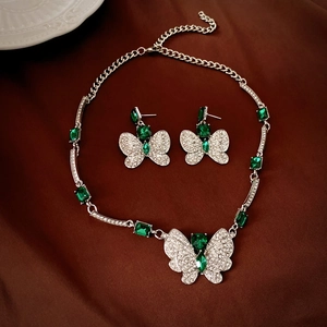 Luxury butterfly necklace and earrings set with emerald green stones on brown satin