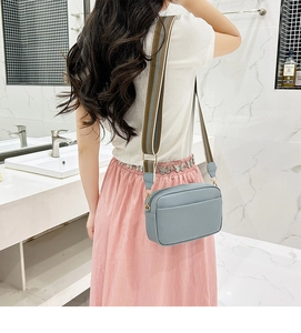 Light blue crossbody camera bag with wide striped shoulder strap shown on model in bathroom