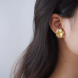 Macro shot of a matte gold flower stud earring on a model's ear with soft shadows