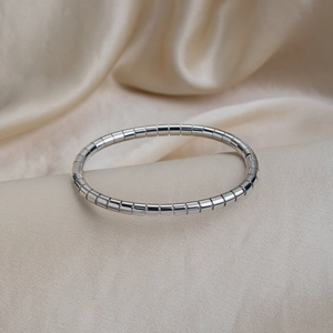 Detailed close-up of polished silver tubogas style elastic bracelet on silk background