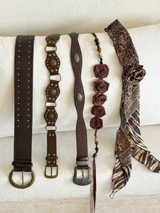 Collection of brown vintage belts with studs and floral waist chains on white fabric