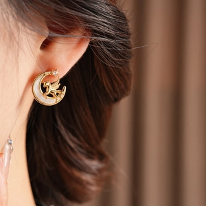 Close-up of golden crescent moon and Pegasus earrings with pearl inlay and crystals