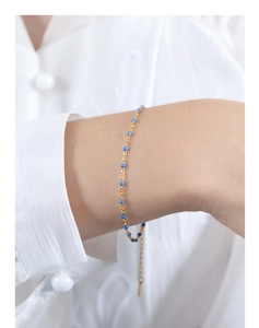 Close-up of a gold chain bracelet with blue beads and adjustable tail on a female wrist