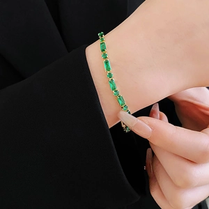 Detalle de pulsera de circonita esmeralda bañada en oro sobre un blazer negro elegante