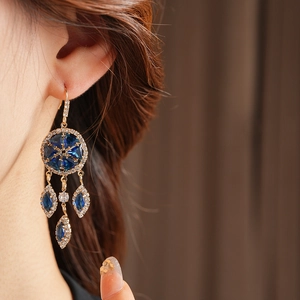 Close-up of vintage gold rhombus earrings with dark blue zircon and tassels on model