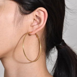 Detail shot of large polished gold hoop earrings worn by a model in minimalist style