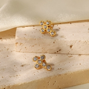 Golden stainless steel cross earrings with sparkling crystals on a stone surface