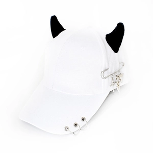 Detail of white baseball cap with black devil horns, metal rings, and safety pin pendant