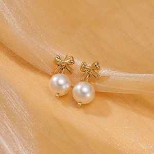 Elegant gold bow earrings with white pearl pendants displayed on golden satin fabric