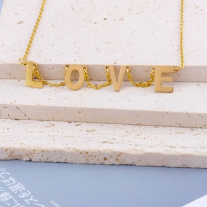 Detailaufnahme einer goldenen LOVE Halskette auf einer natürlichen beige Steinplatte