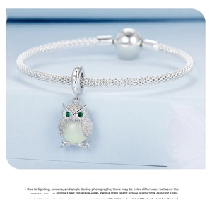 Close-up of owl charm on silver mesh bracelet with glowing stone and green eyes