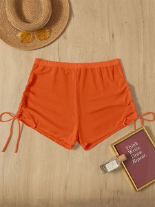 Detail of orange ruched beach shorts with drawstring ties on light wood surface