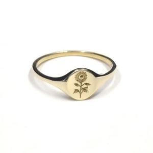 Detail shot of a golden signet ring featuring a finely engraved sunflower on an oval face