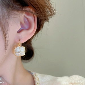 Detail of French vintage gold plated earring with cream enamel and zircon on ear