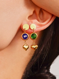 Primer plano de pendientes colgantes dorados asimétricos con cristales azules y verdes y corazones