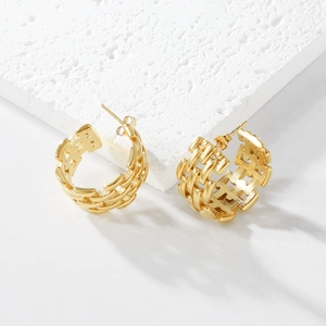 Detailed view of gold plated hollow woven chain pattern earrings on a textured stone base