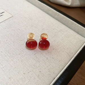 Detailed view of translucent red and amber resin double ball stud earrings on a linen tray