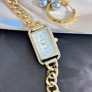 Macro view of a gold square watch with rhinestone bezel and chunky chain strap on silk