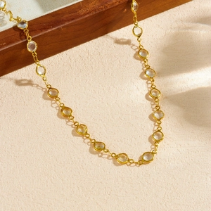 Gold-plated stainless steel necklace with round crystals on a textured beige surface