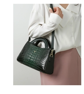 Detail of dark green crocodile pattern handbag with golden V logo and black strap