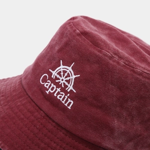 Detail of burgundy washed cotton bucket hat with white Captain embroidery and helm icon