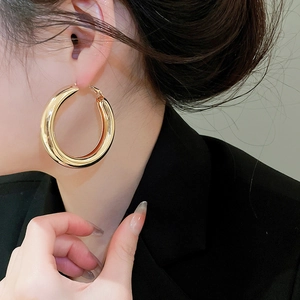 Close-up of a large polished gold hoop earring worn by a model in a black suit