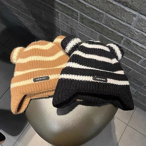 Close-up of striped baby knit hats with cute ears in beige and black on metallic surface