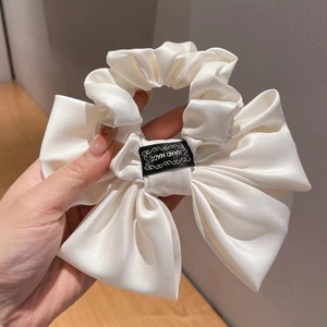 Detail of white satin scrunchie with bow design and hand made tag held by hand