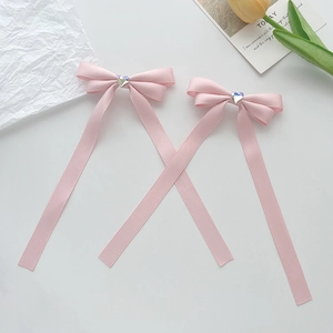 Close-up of pink satin ribbon bow hair clips with heart rhinestone center on white background