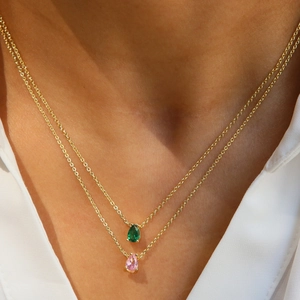 Detail of layered gold necklaces with emerald and pink teardrop zircon pendants