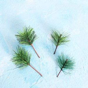 Detail view of four artificial green pine needle sprigs with textured brown stems for crafts