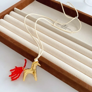 Detail of golden horse pendant with red beaded tail on a cream wax cord necklace
